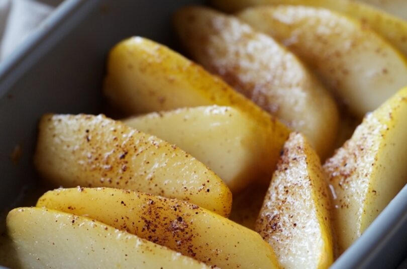 Quartiers de poire rôtis au four pour bébé dès 6 mois, dorés et fondants, saupoudrés légèrement de cannelle, disposés dans un plat adapté aux tout-petits.