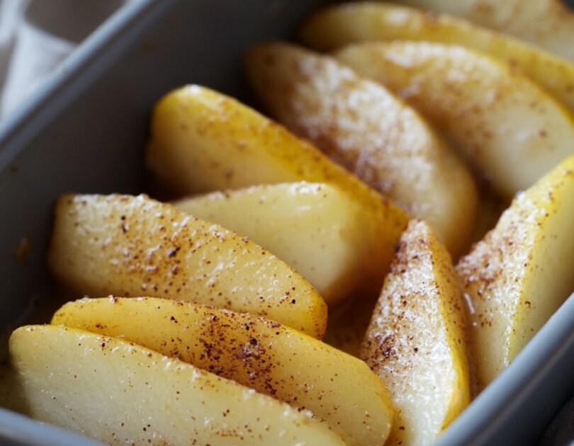 Quartiers de poire rôtis au four pour bébé dès 6 mois, dorés et fondants, saupoudrés légèrement de cannelle, disposés dans un plat adapté aux tout-petits.