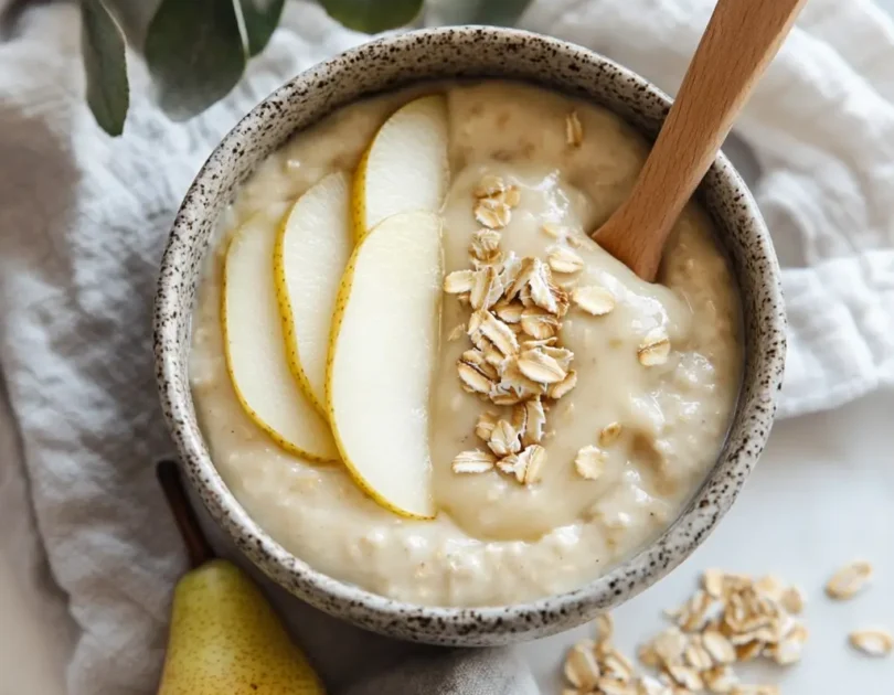 Yaourt nature avec compote de poire et flocons d'avoine pour bébé, présenté dans un bol en céramique avec des tranches de poire fraîche et une cuillère en bois, adapté dès 6 mois.